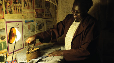 Kenyan woman ironing clothes by the light from a solar lantern